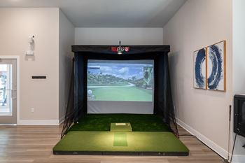 A room with a screen and a golf simulator.